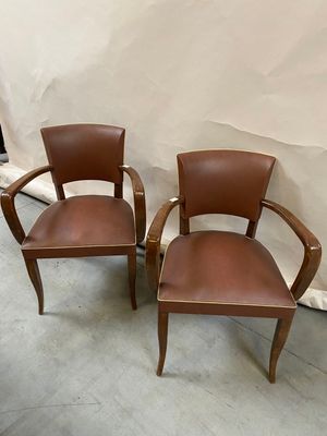 two brown leather chairs sitting next to each other in front of a white wall