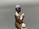figurine of a man sitting on his knees with a hat on