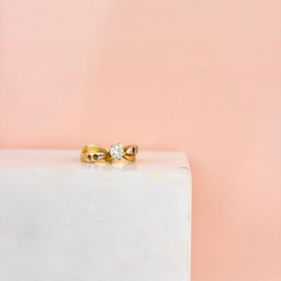 un gros plan d'une bague en or sertie d'un diamant, posée sur un bloc blanc