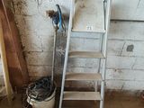une échelle appuyée contre un mur, à côté d'un seau rempli d'outils
