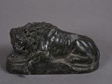 statue of a lion resting on a rock on a gray surface