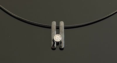 un collier en argent orné d'une pièce, posé sur un fond noir