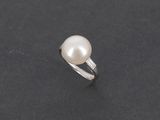une bague en perles blanches et diamants sur une surface noire