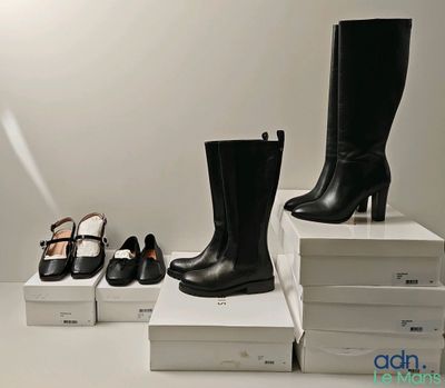Plusieurs paires de chaussures noires et blanches sont posées sur une pile de cartons