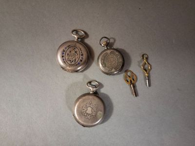 trois montres de poche en argent et une clé posées sur une table