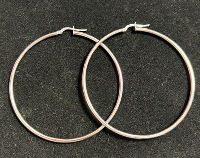 une paire de boucles d'oreilles créoles en argent posées sur une surface noire