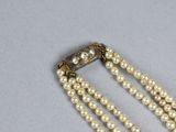 two strands of pearl beads with a gold clasp on a gray surface