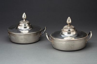 une paire de plats en métal argenté avec couvercles et poignées, posés sur une table