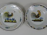 two plates with roosters painted on them sitting on a table