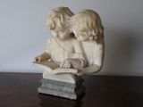 a statue of two children reading a book on a table