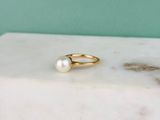 un gros plan d'une bague en or ornée d'une perle, posée sur un bloc de marbre