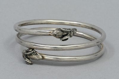 trois bracelets rigides en argent ornés de breloques en forme de poisson, posés sur un fond blanc