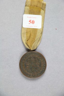 une vieille médaille en bronze entourée d'un ruban, posée sur une surface blanche