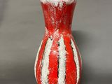 a red and white vase sitting on a gray surface