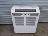 a white air conditioner sitting on the ground next to a garage