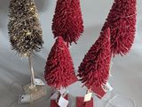 three small christmas trees with red and gold tinsels on a white surface