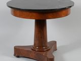 une table ronde avec un plateau en marbre noir reposant sur un piètement en bois