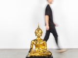 un homme passant devant une statue de Bouddha dorée dans une pièce