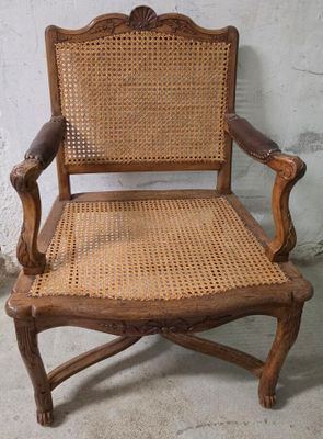 une vieille chaise en bois avec une assise en osier et des accoudoirs, adossée à un mur blanc