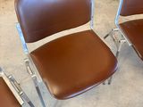 Quatre fauteuils en cuir marron sont disposés en cercle sur un sol en béton