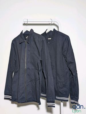 two jackets hanging on a clothes rack in front of a white wall