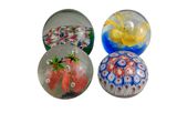 quatre presse-papiers en verre de couleurs et de motifs différents sur fond blanc