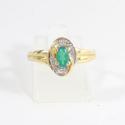 gros plan d'une bague en or avec une pierre verte et des diamants