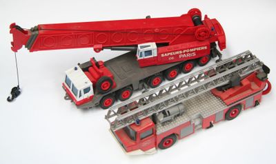 un camion de pompiers miniature et une grue miniature posés sur une surface blanche