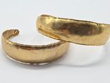 two gold cuff bracelets on a white surface