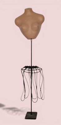 un mannequin posé sur un socle noir, avec un fond rose pâle