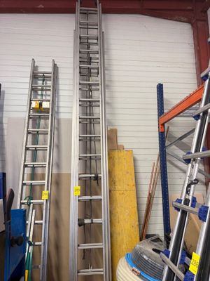 Plusieurs échelles sont alignées dans un garage, dont une appuyée contre le mur.