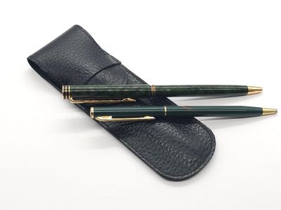 deux stylos verts et un étui noir posés sur une surface blanche