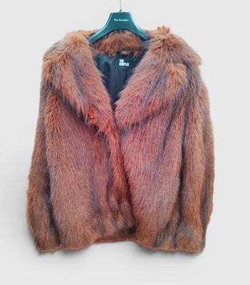 un gros plan d'une veste en fourrure rose suspendue à un cintre