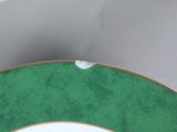 a green and white plate with gold trim on a table