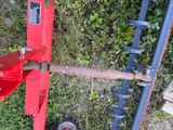a red plow sitting on the ground next to some bushes