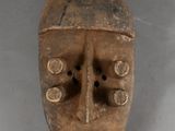 an old wooden mask hanging on a wall on a gray surface