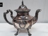a silver tea pot on a stand on a white table