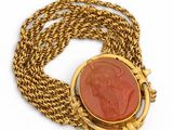 a close up of a gold necklace with a red stone in the center