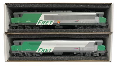 Deux trains miniatures se trouvent dans une boîte posée sur une surface blanche