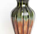 a green and brown vase sitting on a white surface
