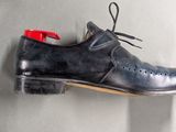 pair of black leather shoes hanging on a wall with a red shoelacer