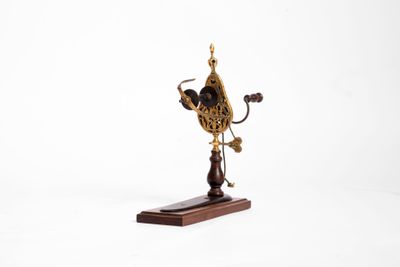 une petite horloge posée sur un socle en bois, sur fond blanc
