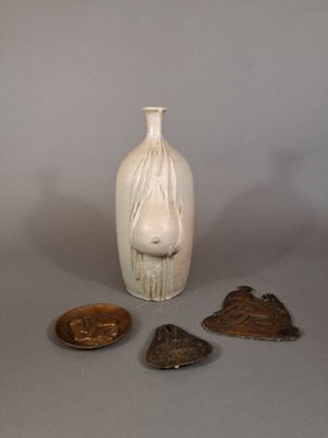 un vase blanc orné d'un visage, à côté de trois autres objets
