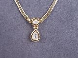 a close up of a gold necklace with a tear shaped diamond