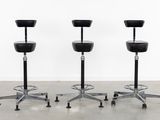 three black stools sitting on top of each other in front of a white wall