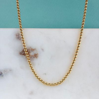 un collier de perles dorées posé sur un comptoir en marbre