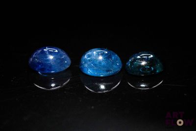 three blue and one green gems sitting on top of a black surface
