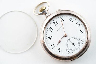 une montre de poche en argent posée à côté d'un verre de vin