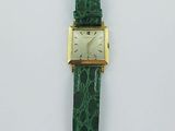a close up of a watch with a green strap on a white surface