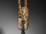 un masque en bois muni de cornes, posé sur un socle